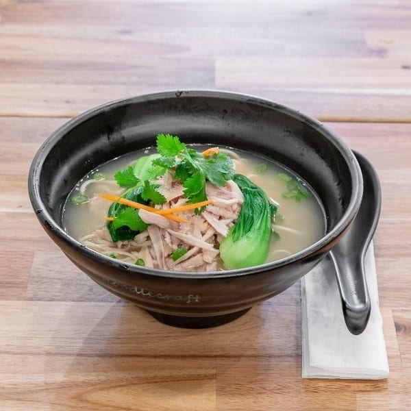 Chicken noodle soup with bok choy, cilantro, and shredded carrots in a black bowl.
