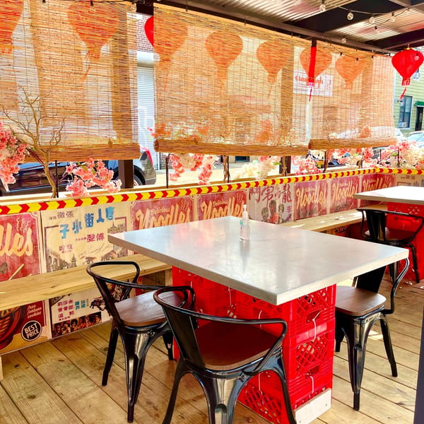 Outdoor dining area with bamboo blinds, red lanterns, cherry blossoms, and tables made from red crates.