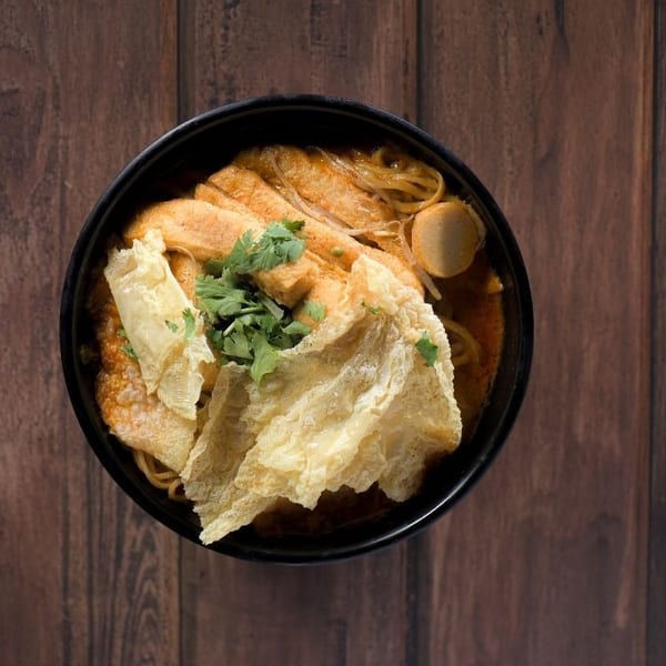 Overhead view of a black bowl filled with curry noodles, tofu, fish cakes, and cilantro.