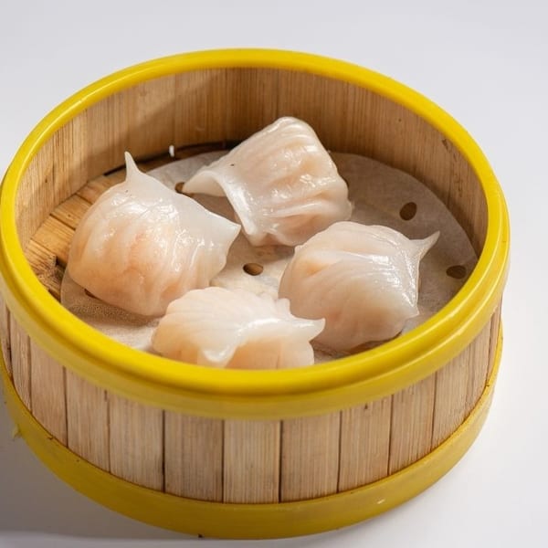 Four translucent shrimp dumplings (har gow) in a bamboo steamer basket on a white background.