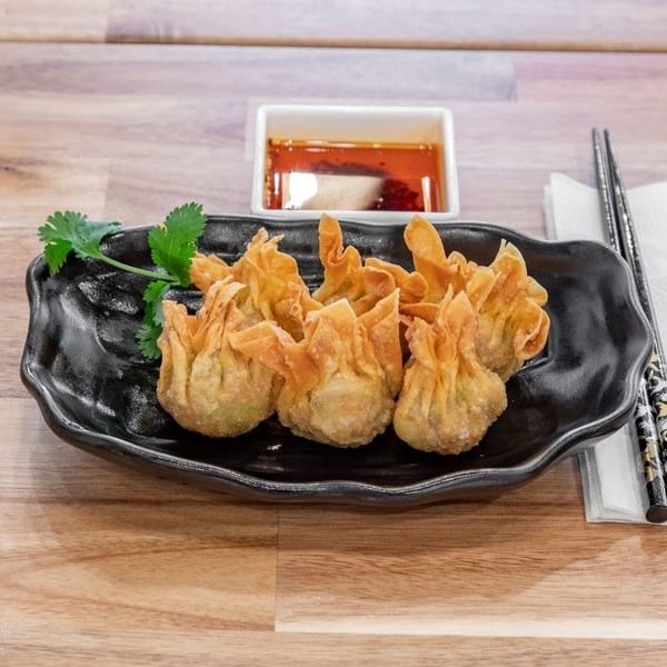 Crispy fried wontons on a black plate with cilantro, chili oil, and chopsticks on a wooden table.